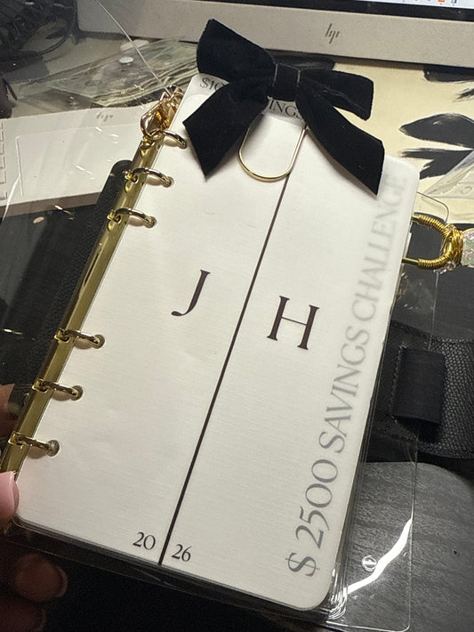 Small notebook with a black bow and gold accents held by a hand, with a blurred background.