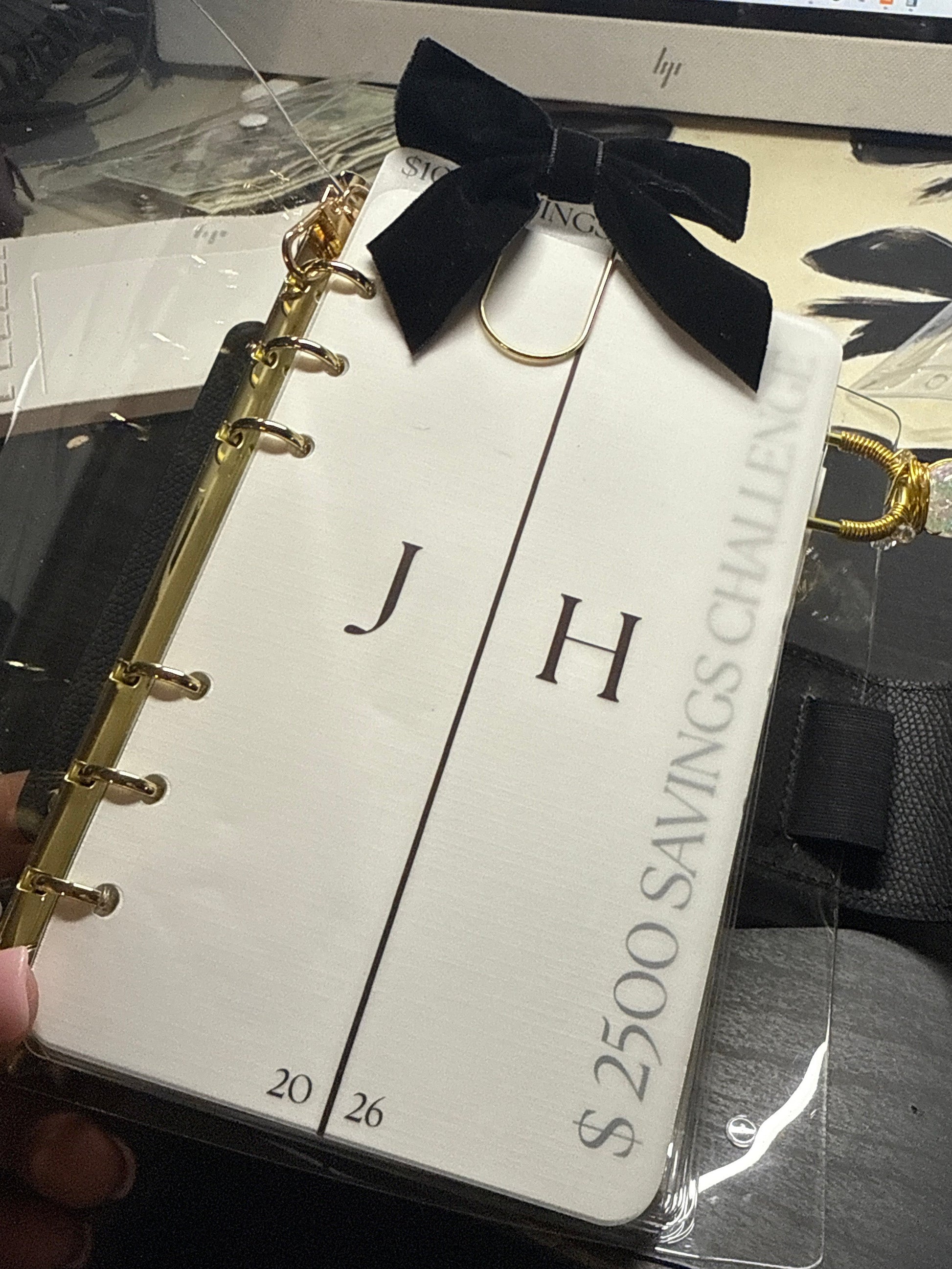 Small notebook with a black bow and gold accents held by a hand, with a blurred background.